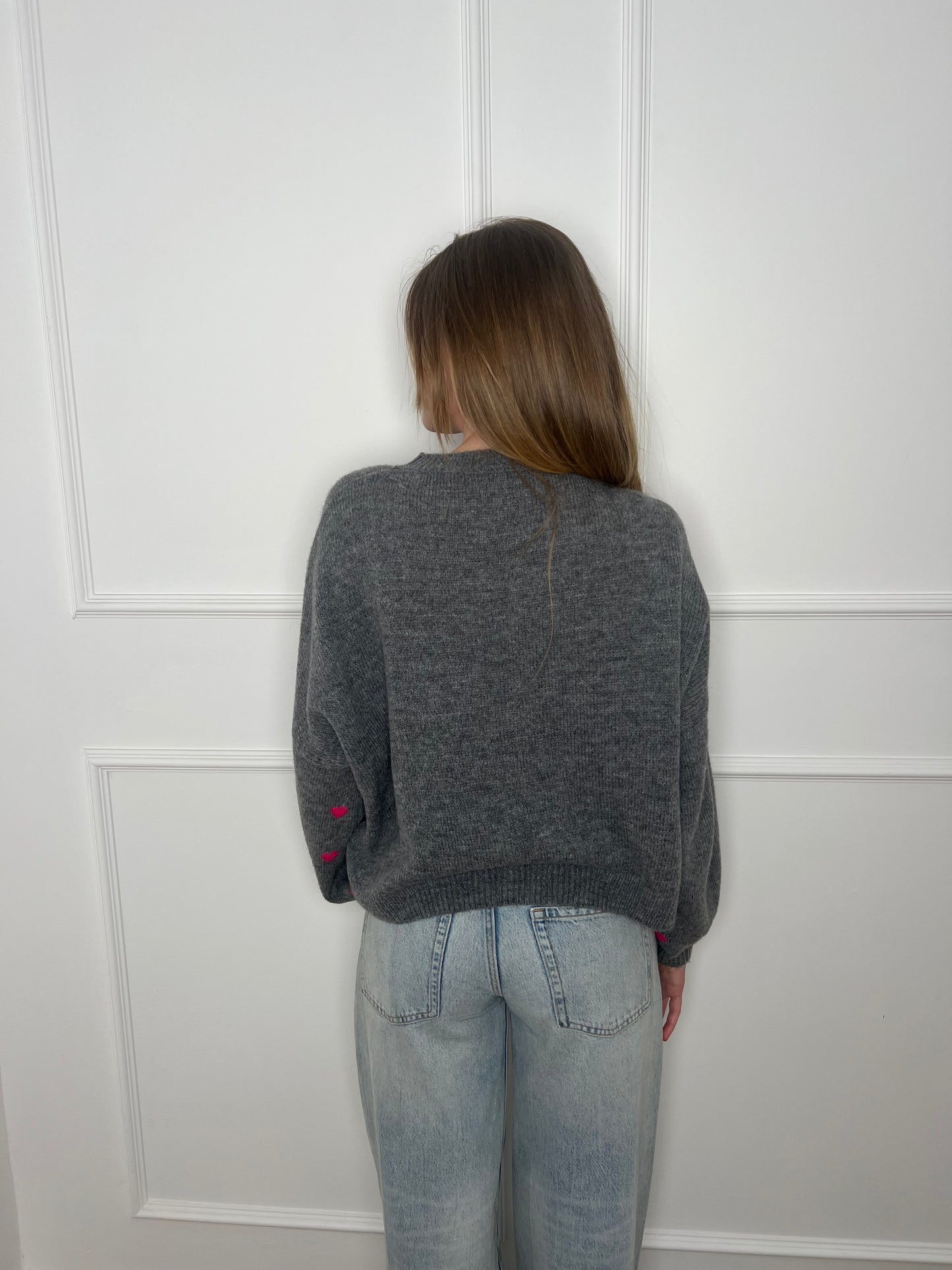 Frau vor weißer Wand von hinten trägt einen grauen Pullover