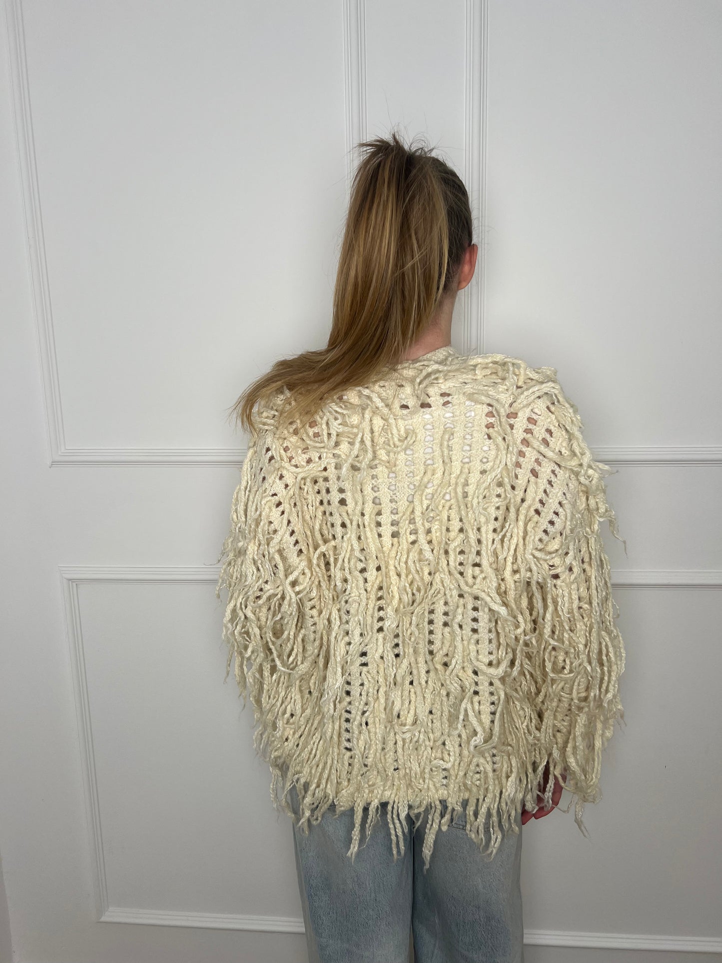 Frau von hinten vor weißer Wand trägt eine weiße Zottel Strickjacke