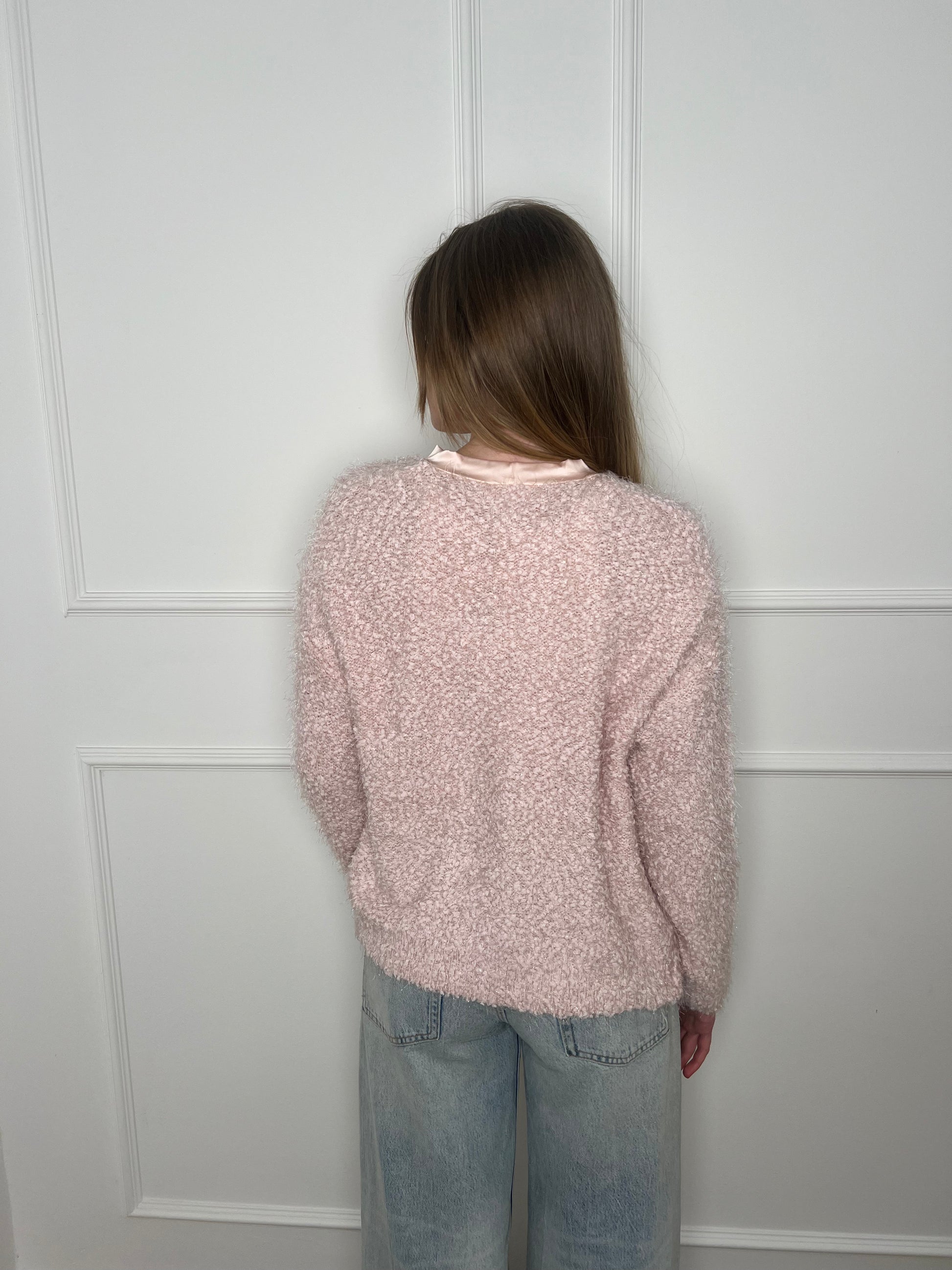 Frau von hinten vor weißer Wand trägt einen rosanen Cardigan
