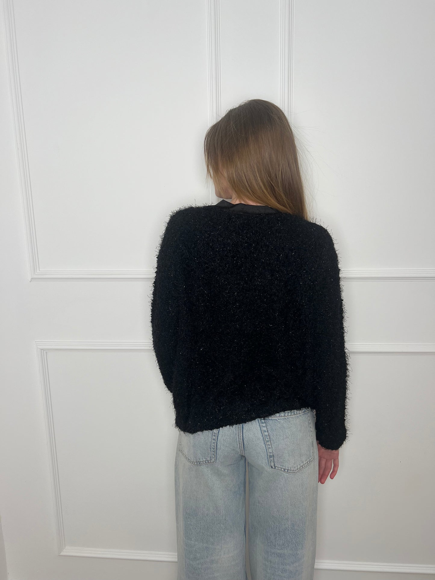Frau vor weißer Wand von hinten trägt einen schwarzen Cardigan