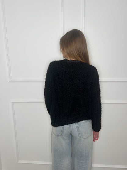 Frau vor weißer Wand von hinten trägt einen schwarzen Cardigan