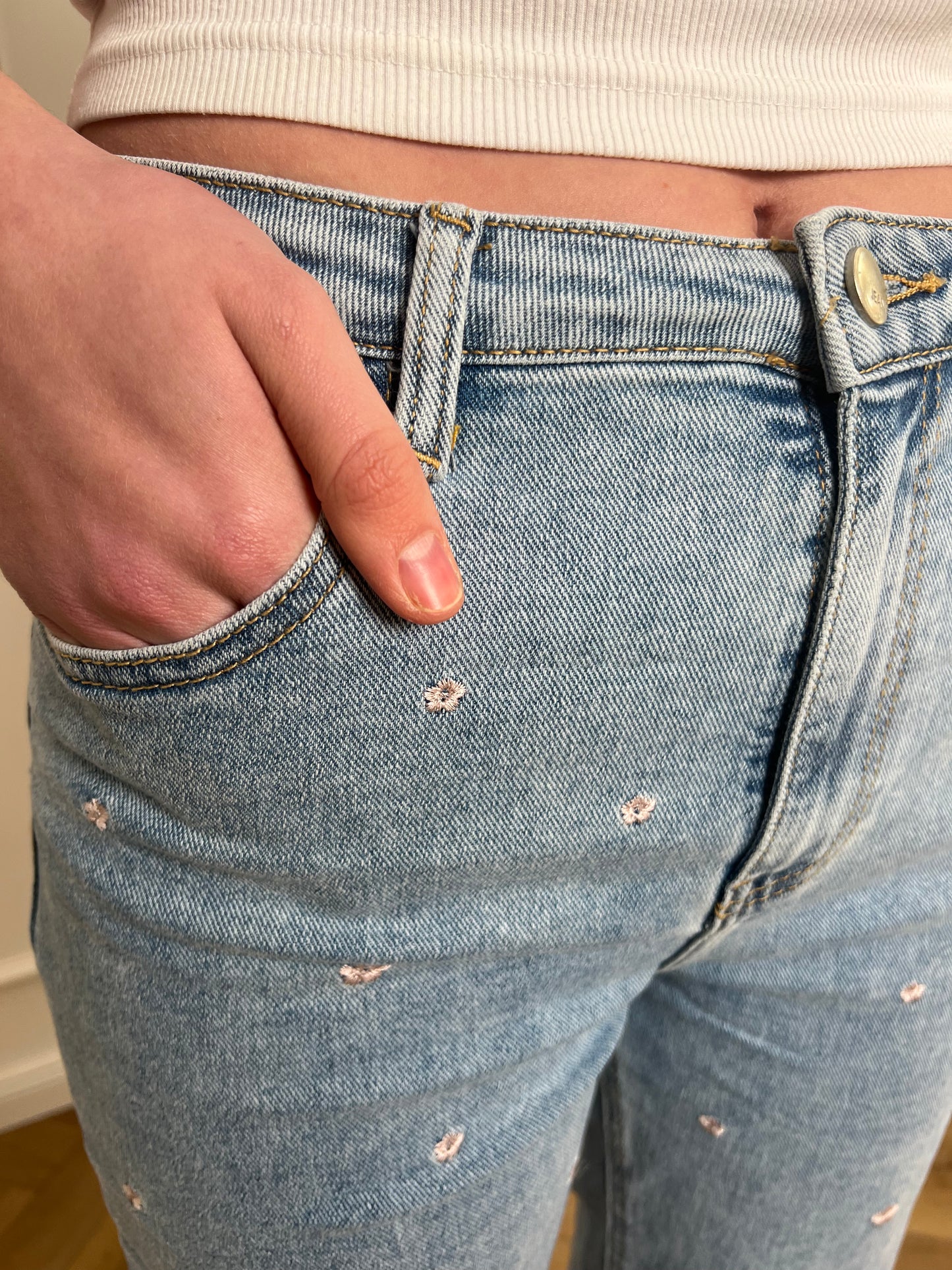 Jeans mit Blumenmuster in Nahaufnahme von der Hosentasche, in die eine Frauenhand gesteckt wird