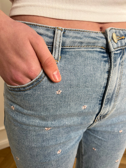 Jeans mit Blumenmuster in Nahaufnahme von der Hosentasche, in die eine Frauenhand gesteckt wird