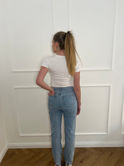 Frau von hinten vor weißer Wand trägt eine Jeans mit Blumenmuster