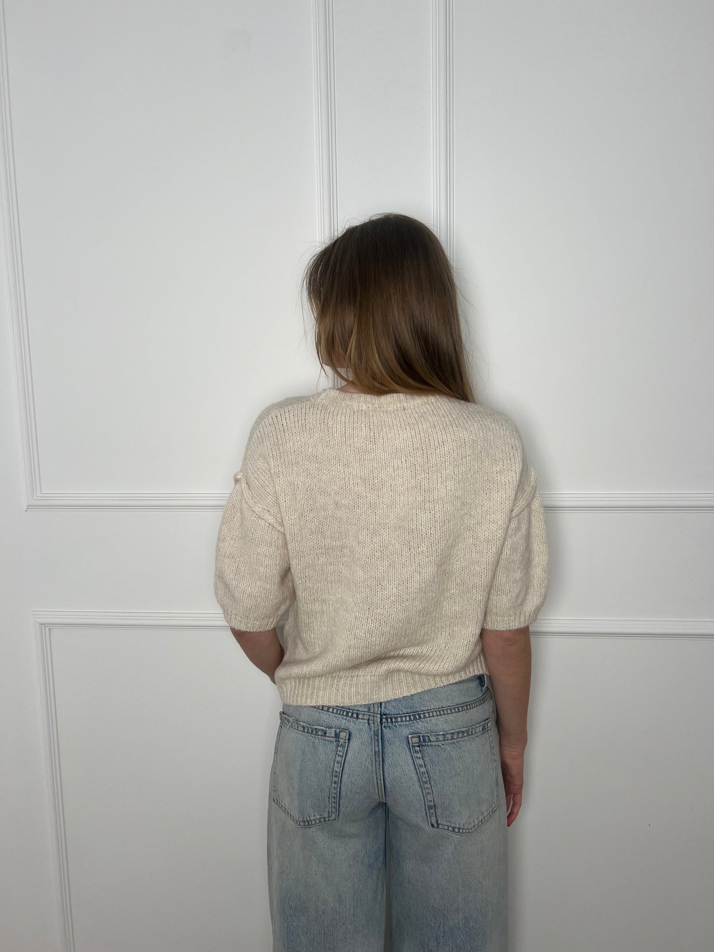 Frau von hinten vor weißer Wand trägt einen weissen Pullover mit kurzen Armen.
