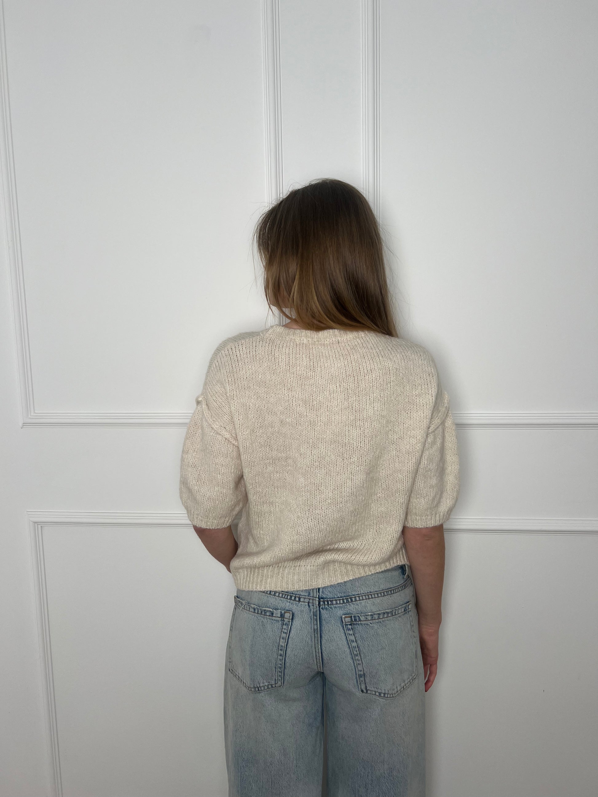 Frau von hinten vor weißer Wand trägt einen weissen Pullover mit kurzen Armen.