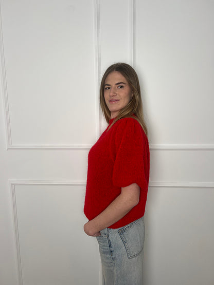 Frau von der Seite vor weißer Wand trägt einen roten Pullover mit kurzen Armen.