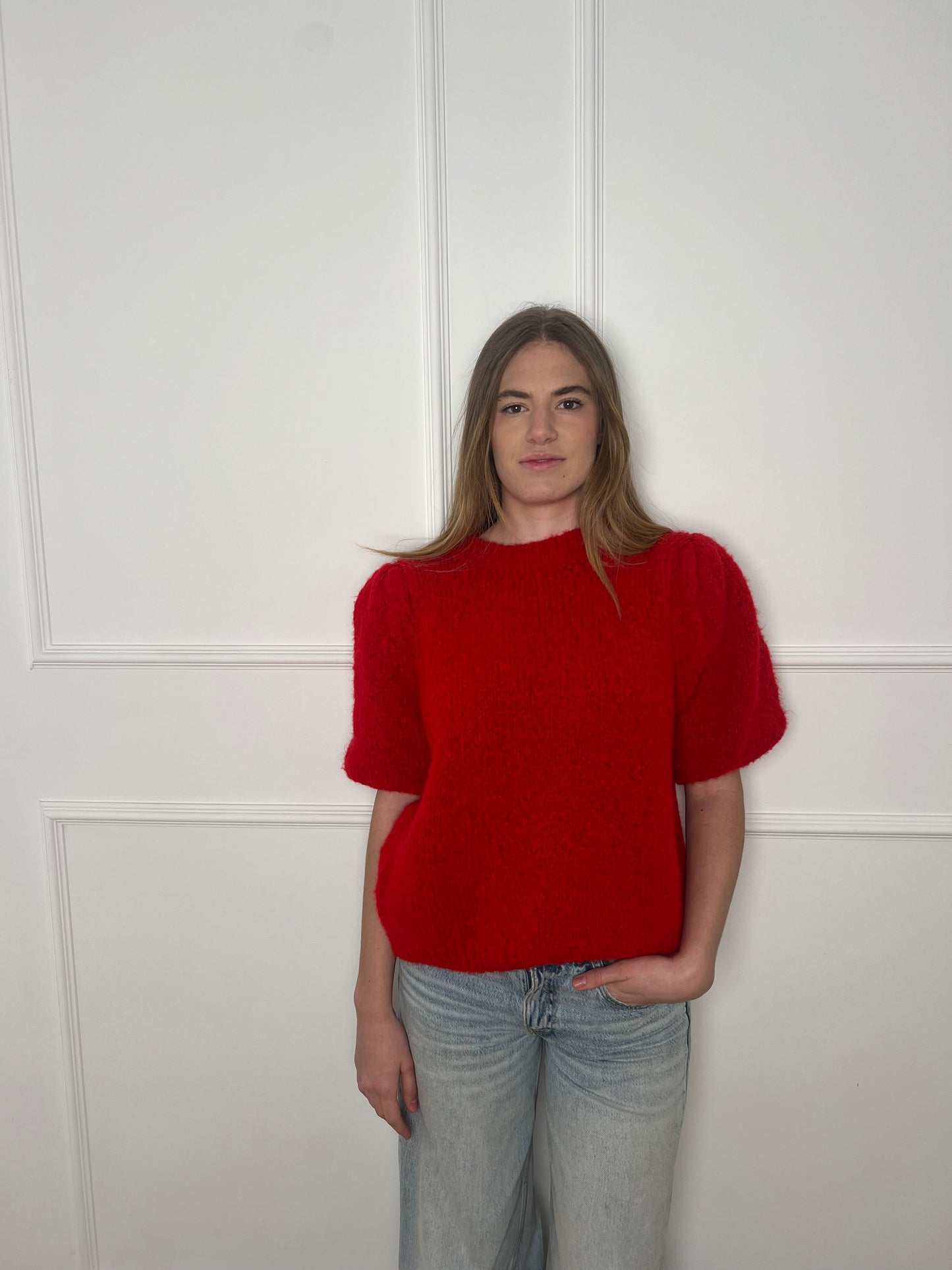 Frau vor weißer Wand trägt einen roten Pullover mit kurzen Armen.
