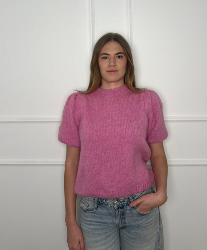 Frau vor weißer Wand trägt einen pinken Pullover mit kurzen Armen.