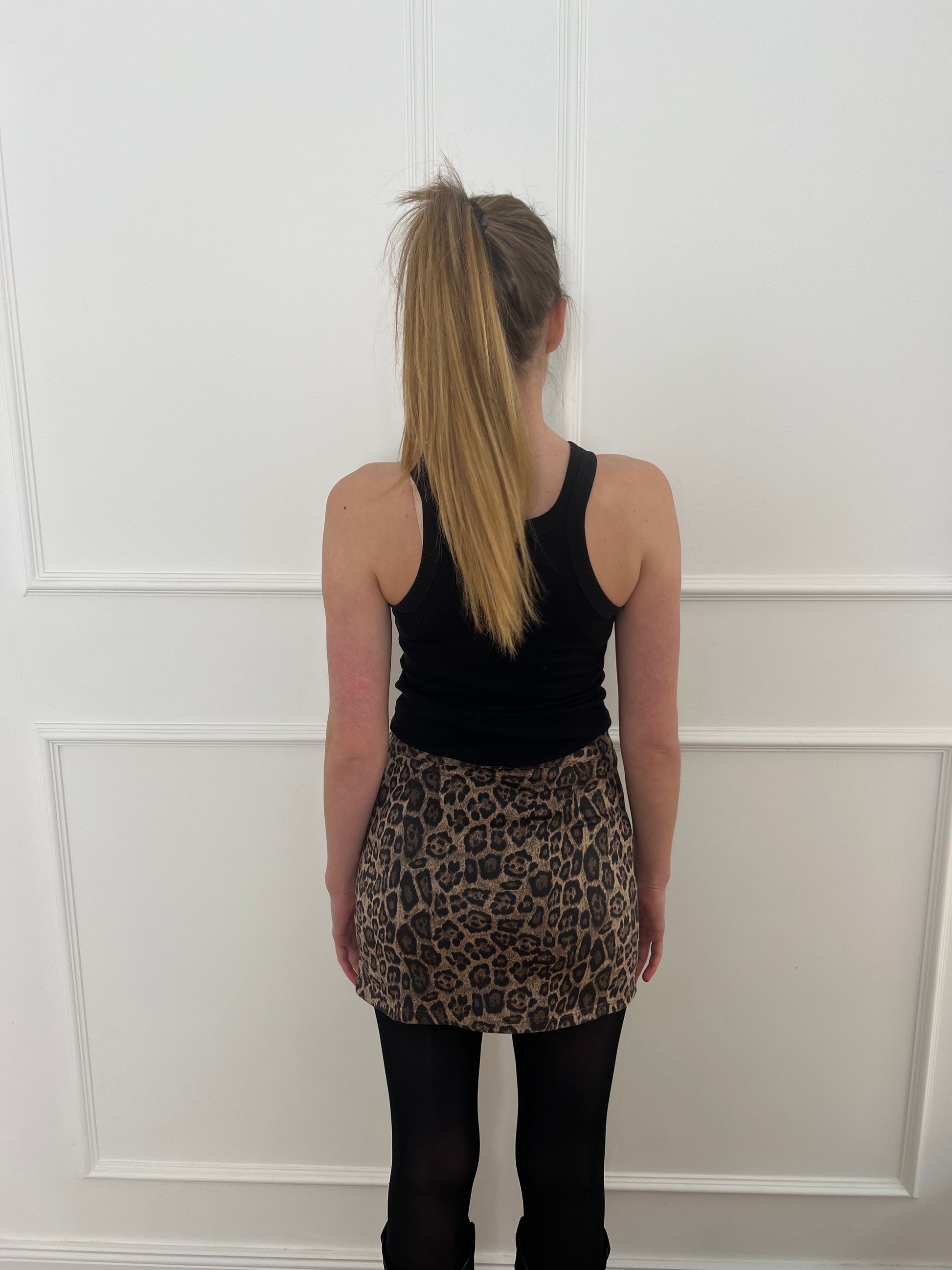 Frau von hinten vor weißer Wand trägt einen Rock im Leoprint