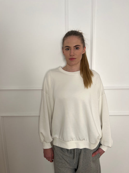 Frau vor weißer Wand trägt ein weißes Sweatshirt mit langem Arm.