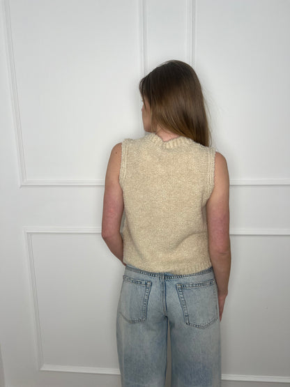 Frau vor weißer Wand trägt eine Weste in beige und ist von hinten zu sehen.