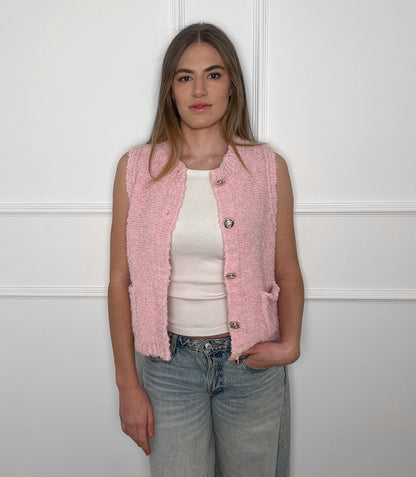 Blonde Frau vor weißer Wand, die eine rosafarbene Weste und darunter ein weißes Top trägt