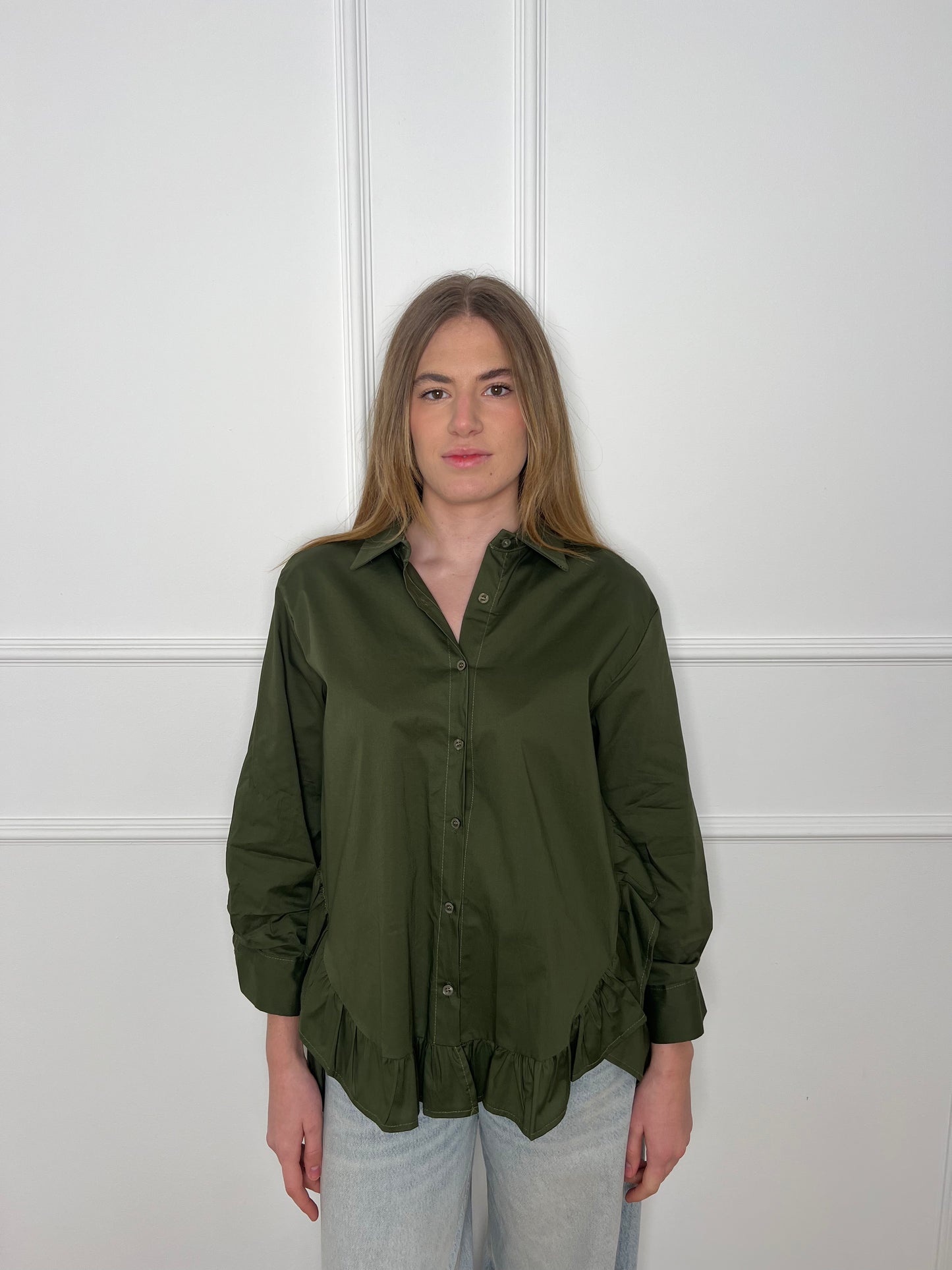 Blonde Frau vor weißer Wand trägt eine olivgrüne Bluse