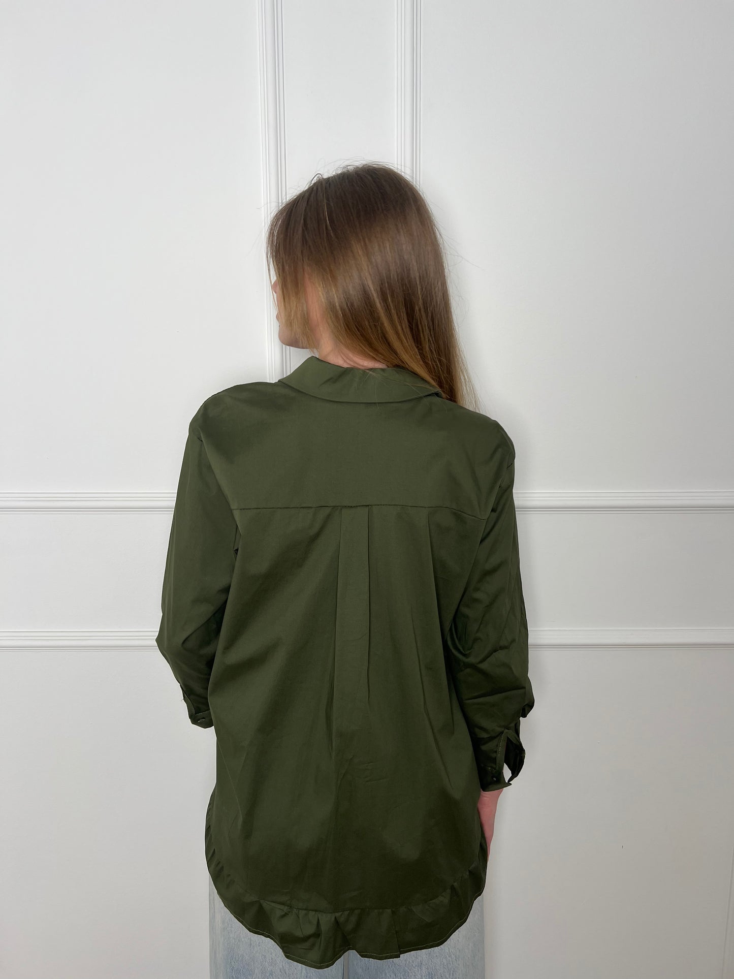 Blonde Frau vor weißer Wand trägt eine olivgrüne Bluse