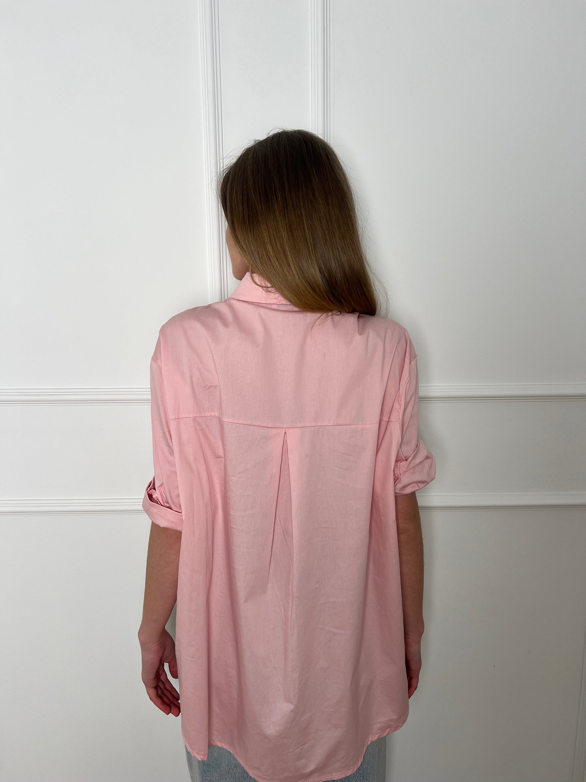 Blonde Frau vor weißer Wand trägt eine rosafarbene Bluse