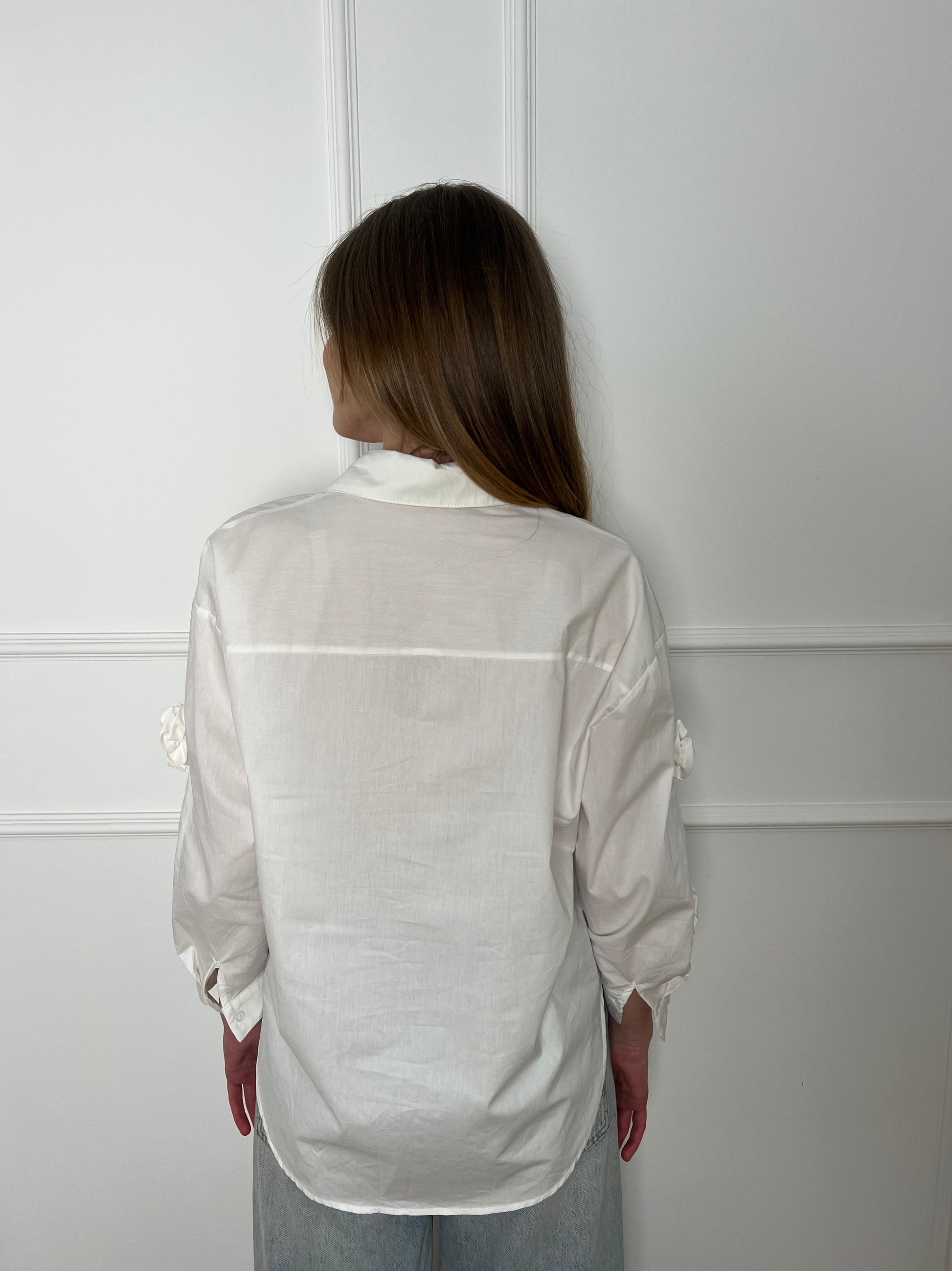 Blonde Frau vor weißer Wand trägt eine weiße Bluse