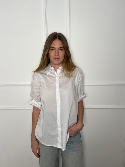 Blonde Frau vor weißer Wand trägt eine weisse Bluse