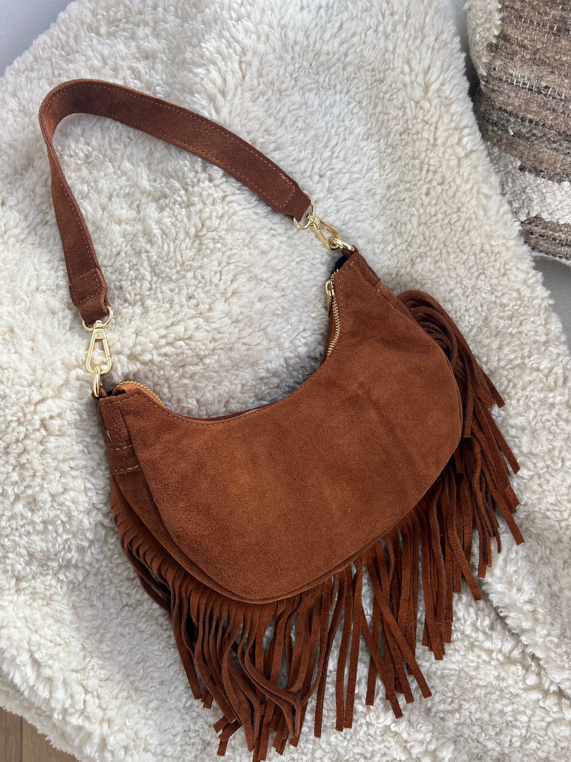 Braune Festivaltasche mit Fransen liegt auf weißem Stoff.